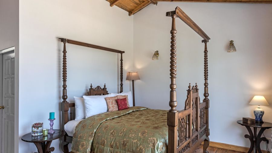 Side view of the  Superior Room  bed with wooden frames and lamp placed on the side of the room at Te Aroha by Shervani Mukteshwar