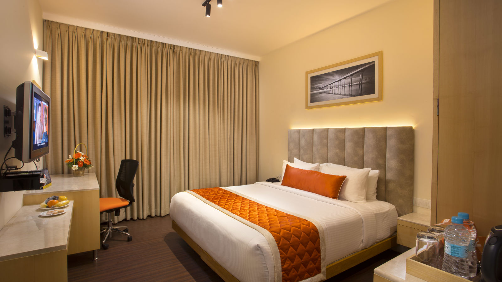 A cosy hotel room with a plush bed adorned with an orange bed runner, a work desk and a wall-mounted TV - Hotel Langford Keys by TGI, Shanti Nagar