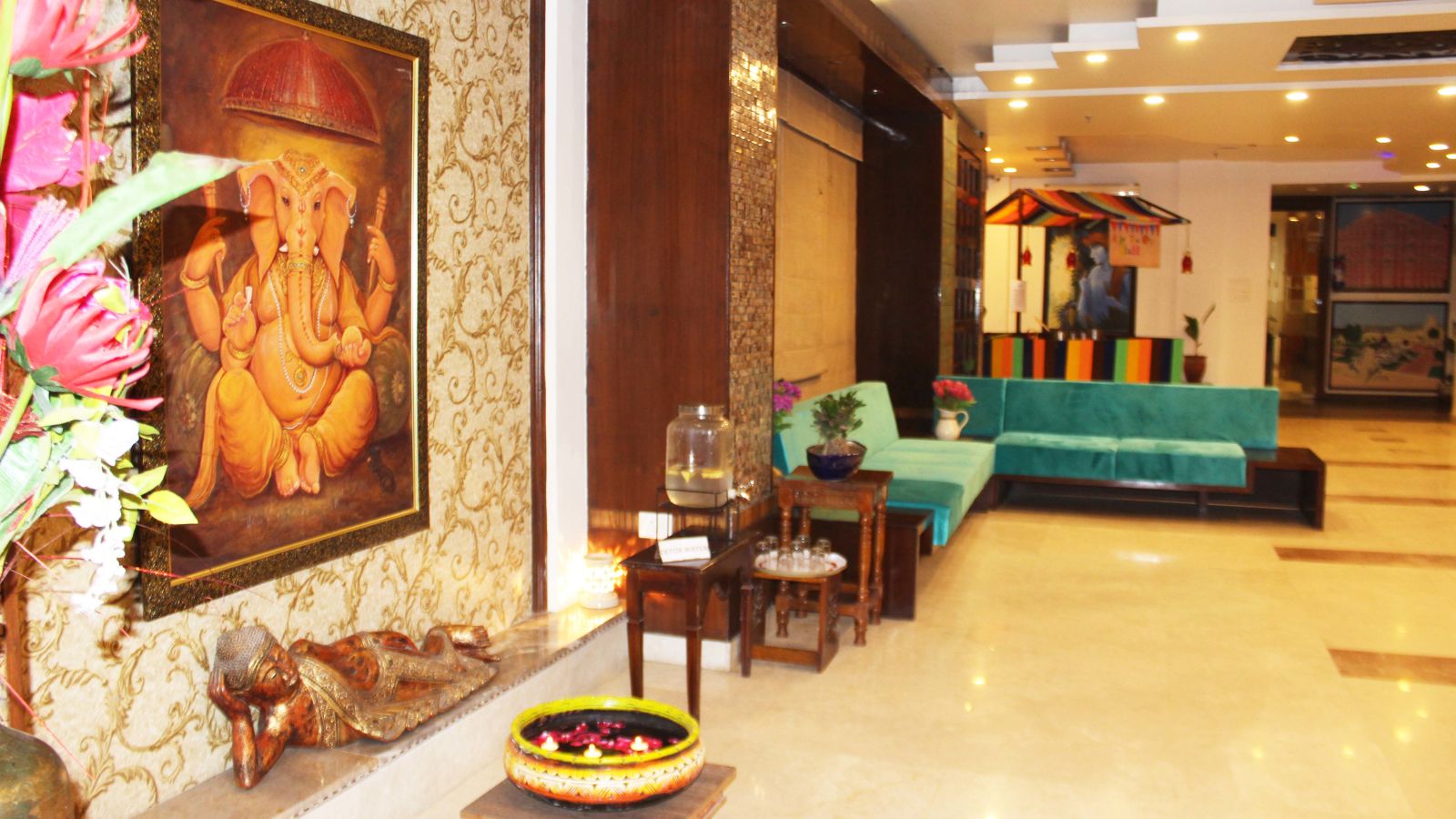 A warmly lit tiled lobby of the hotel with comfortable sofas and a painting of the lord Ganesha on the wall  - TGI Apple Inn, Jaipur 