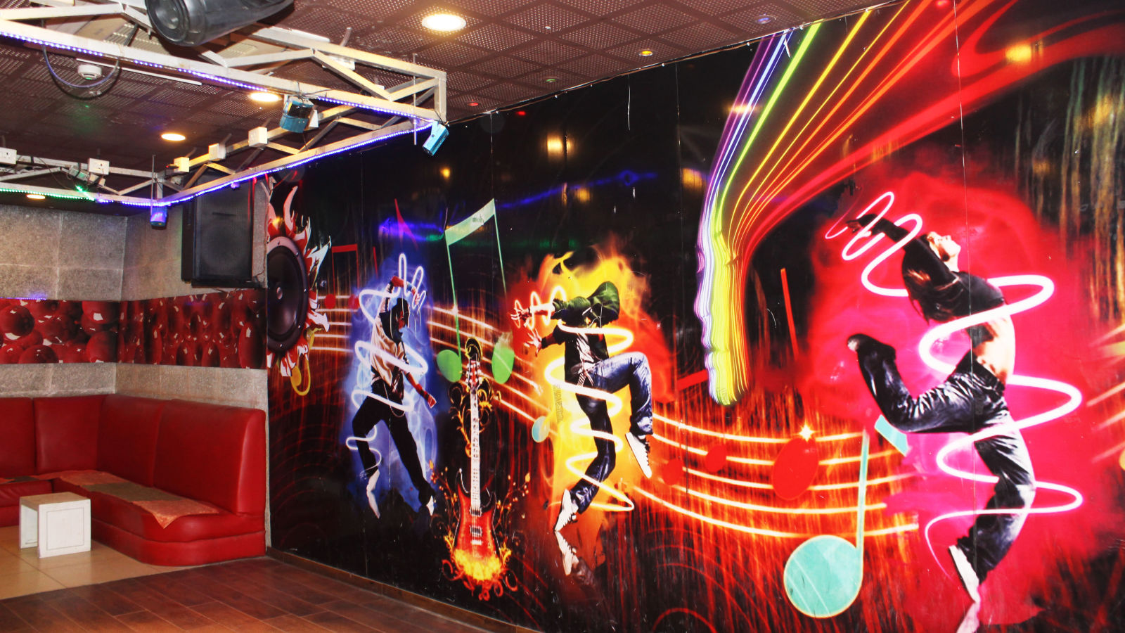 A dance club with vibrant wall murals of dancers, a red tufted sofa and disco lighting - TGI Apple Inn, Jaipur 