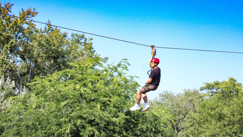 a man on a zip line surrounded by greenery - Adventure Park near Ahmedabad