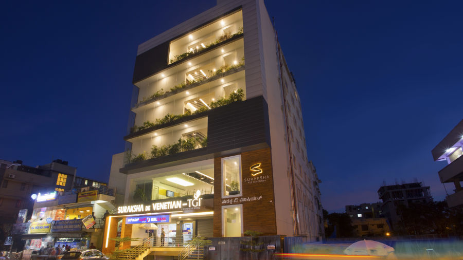 An exterior view of a modern multi-story building illuminated at dusk with signage and street activity - De Venetian by TGI, Brookefield