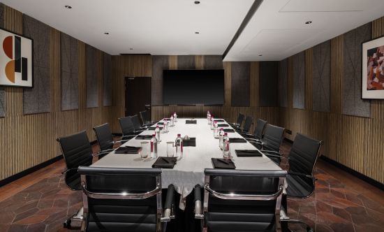 alt-text A conference room with dark walls, a long table, and chairs arranged around it, at Parallel Hotel Udaipur.