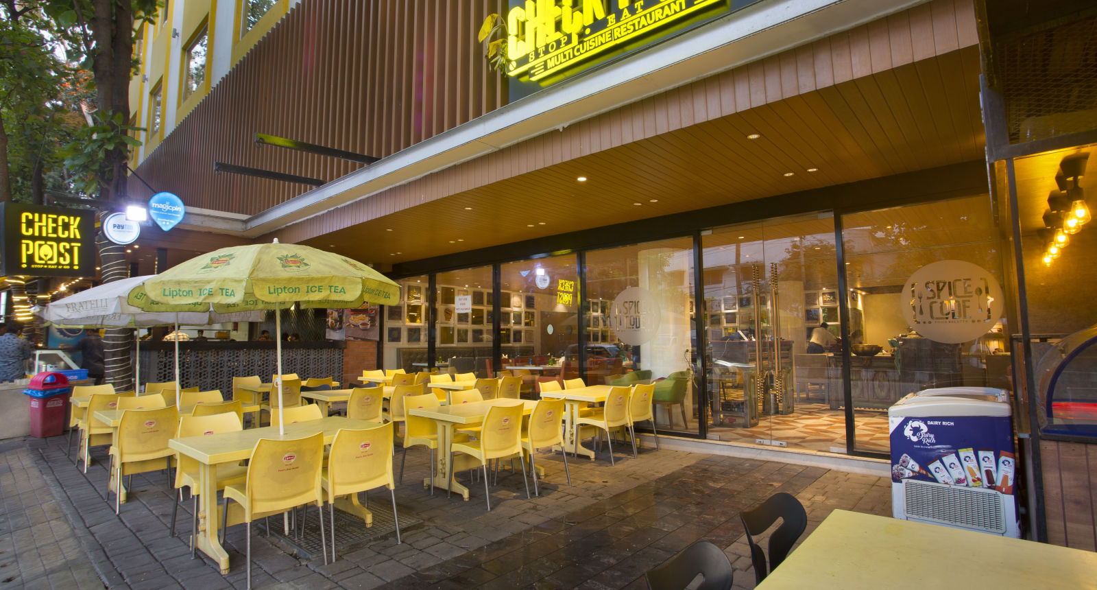 an outdoor restaurant with umbrellas mounted on the tables to provide shade - Hotel Fountain Tree By TGI - JP Nagar, Bangalore