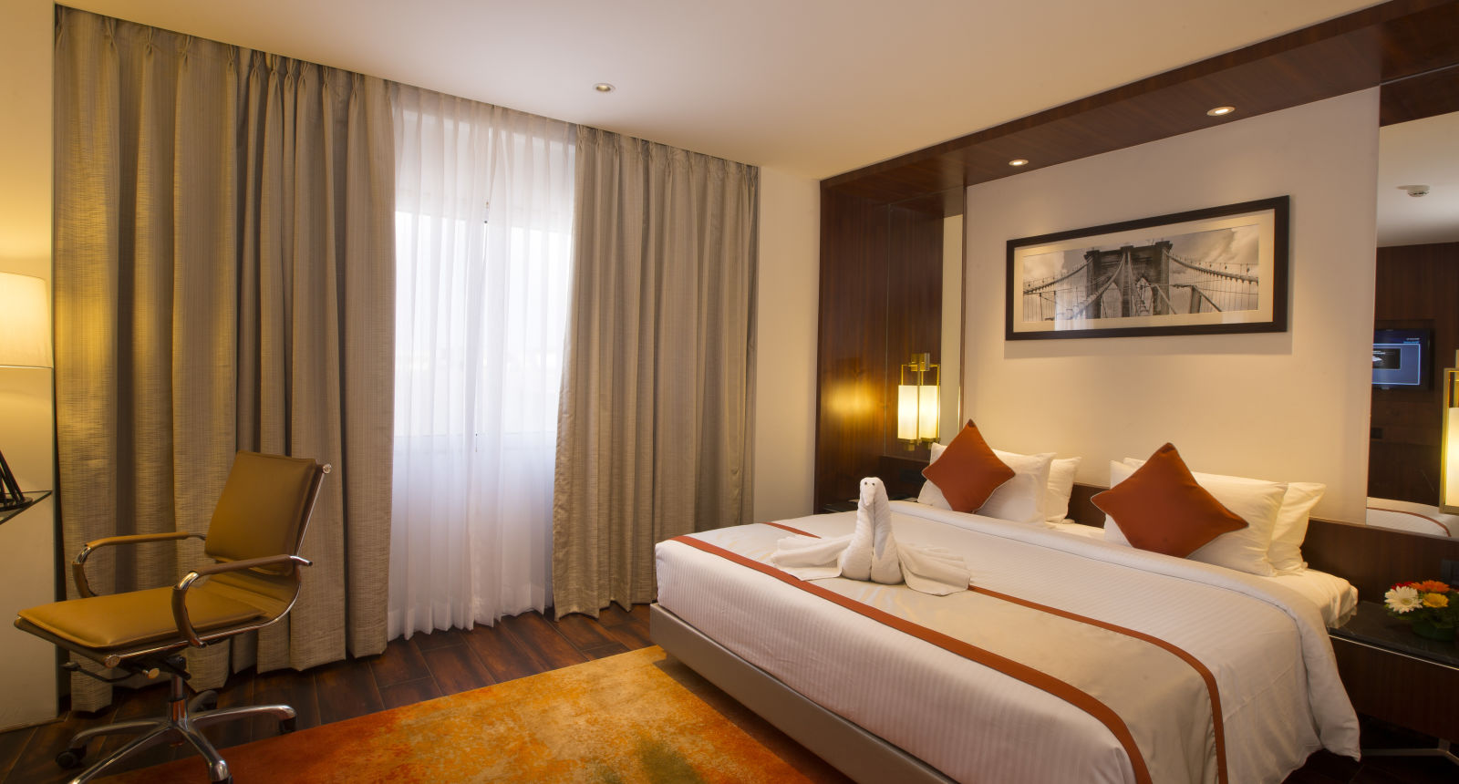 Another view of a hotel room with a large bed with white and orange linens, a brown office chair and sheer curtains over a window - Hotel Southend by TGI - Bommasandra, Bangalore