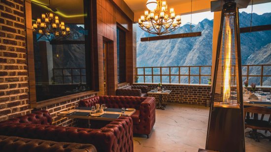 brown couches placed against a brick wall overlooking the lush green mountains of Himalayas atThe Tattva Boutique Resort, Joshimath