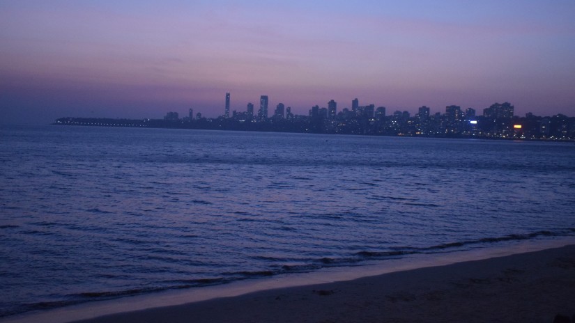 reflection of sky in shades of blue after sunset in the sea water by Juhu Beach with skyscrapers in the background