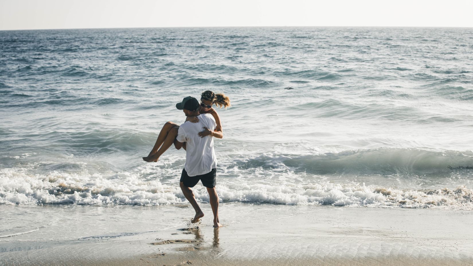 a couple having fun at the beach while the man has lifted the woman i his arms with the cool breeze brushes through their hair