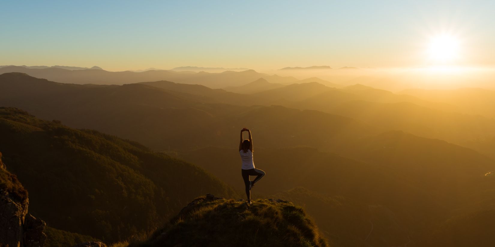 a person practicing yoga on hilltop during sunrise