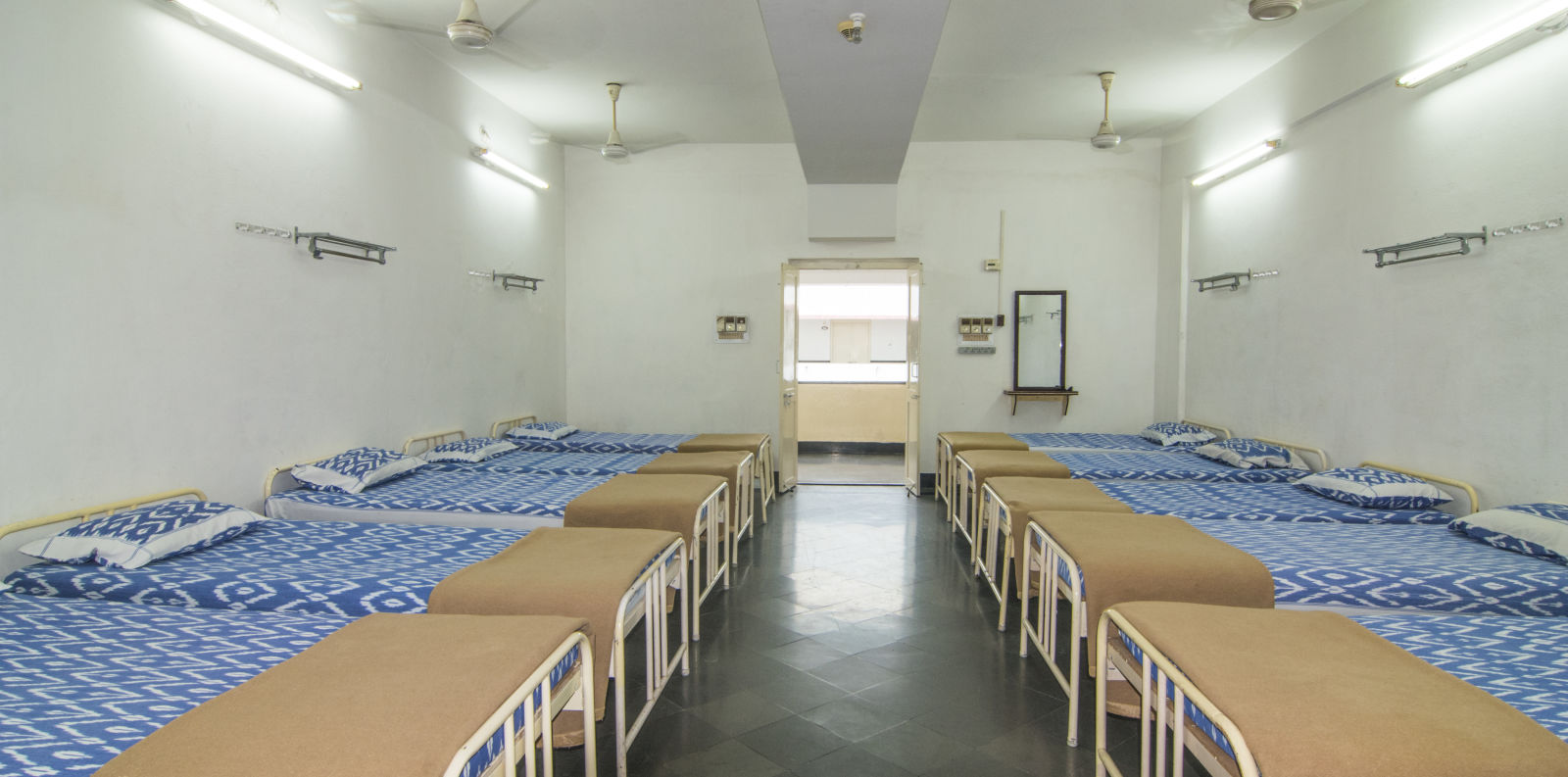 A full view of beds with bedding arranged in two rows in a room | Hotel Sahara