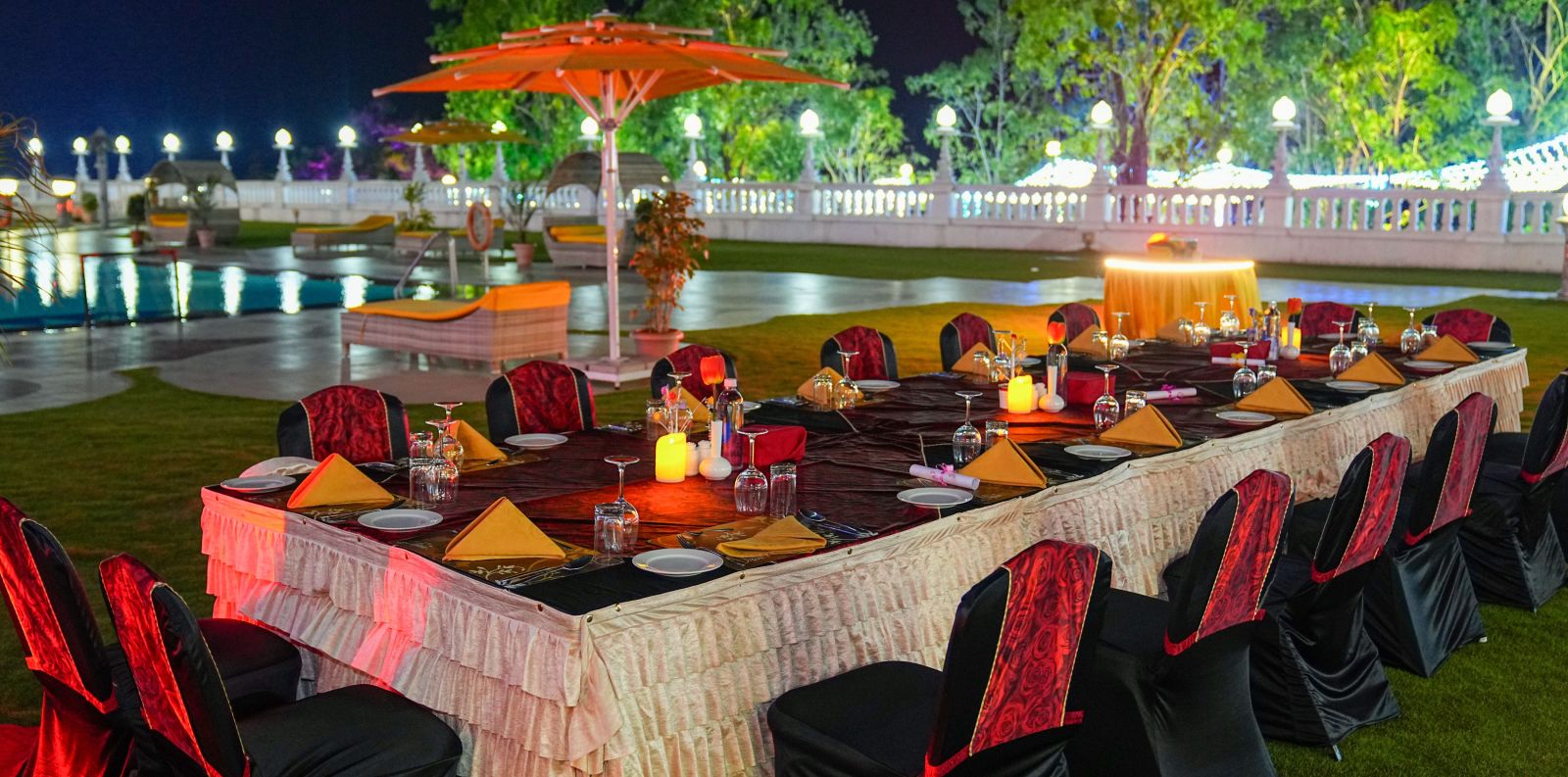 a set banquet table on a lawn with a swimming pool in the background at night