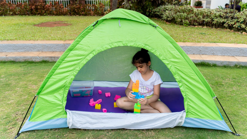 a kid playing with building blocks inside a tent placed on the lawn