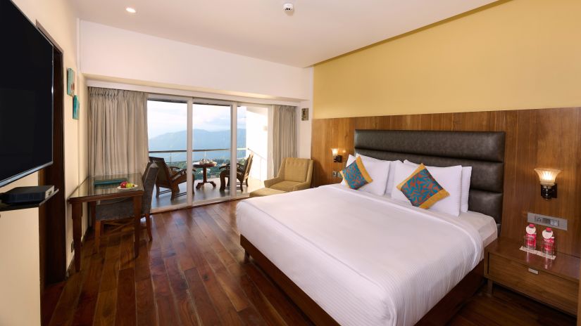 A room featuring a bed, a side drawer, a TV and a balcony with seating arrangements - Renest Dunsvirk Court Mussoorie