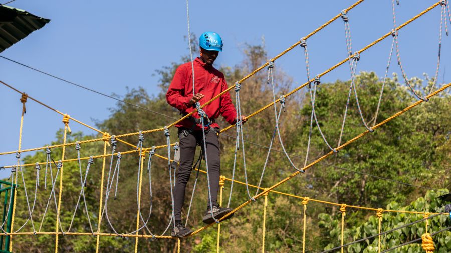 Participant walking on a suspended rope bridge as part of an adventure activity. | Stone Wood Jungle Resort, Dandeli