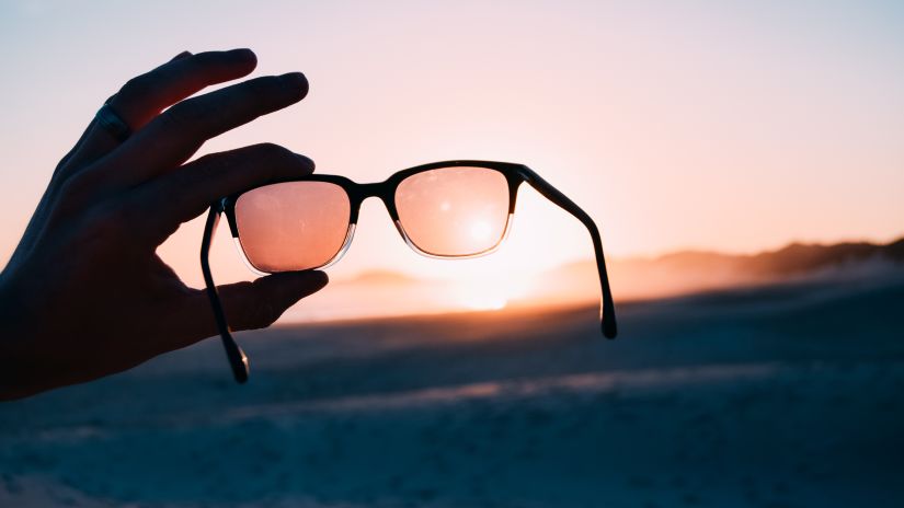 a person showing their sunglasses with the sun set in the background