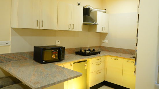 A kitchen with a microwave, a cooking stove, a chimney and storage cabinets - A M Suites