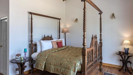 Side view of the  Superior Room  bed with wooden frames and lamp placed on the side of the room at Te Aroha by Shervani Mukteshwar