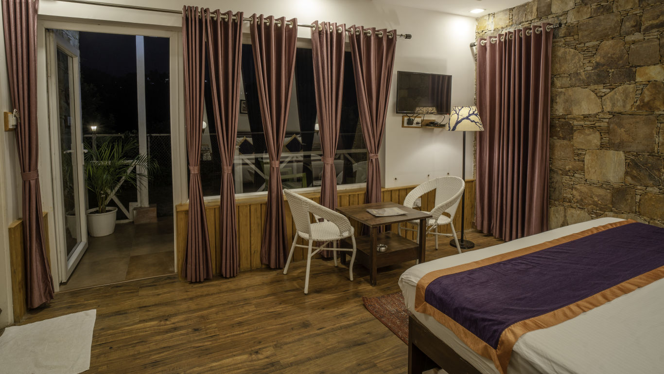 A room with a bed, chairs, a table, a TV and a balcony area -  The Nature's Green Resort, Bhimtal
