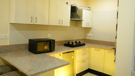 A kitchen with a microwave, a cooking stove, a chimney and storage cabinets - A M Suites