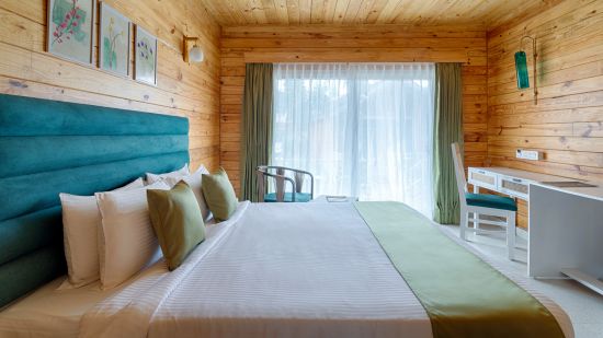 A warm, inviting bedroom featuring a large bed with a teal headboard and sage green accents, flanked by wooden walls and a sheer curtained window Aralea Beach Resort by Stone Wood, Morjim