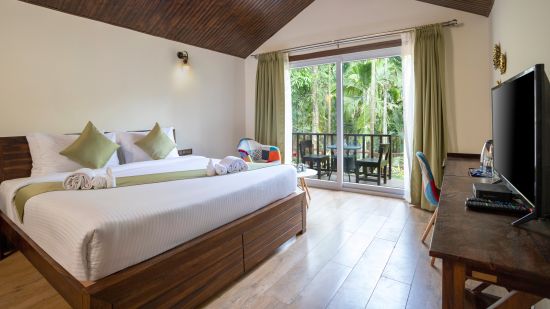 A room in our resort with a large bed with green pillows in front of a television - Stone Wood Nature Resort, Gokarna