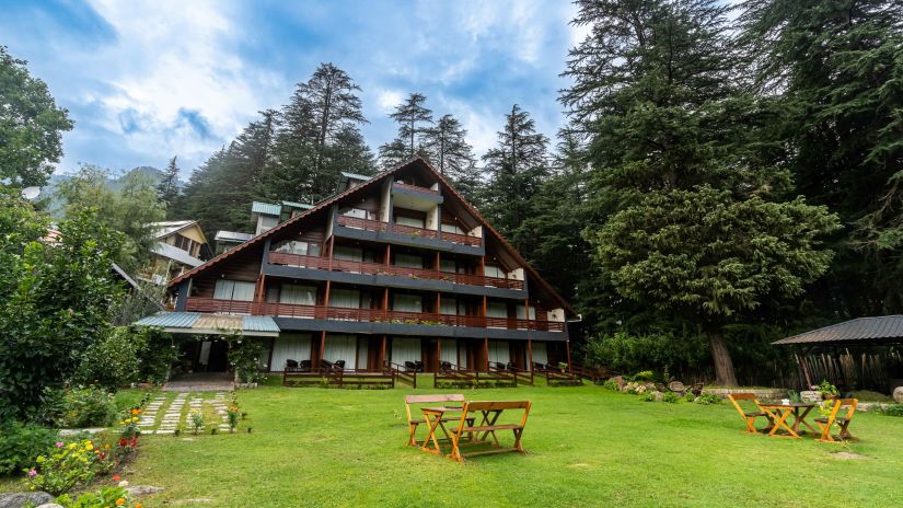 Facade of Bedzzz Xclusiv Baikunth, Manali with sitting area in front of it and surrounded by trees