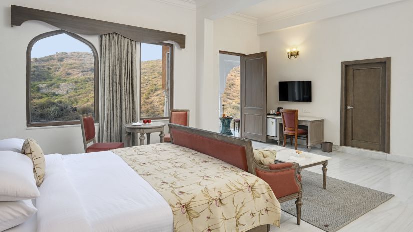 Fateh Vilas Udaipur - interior view of the suite featuring a king size bed a work desk a television and windows with curtains