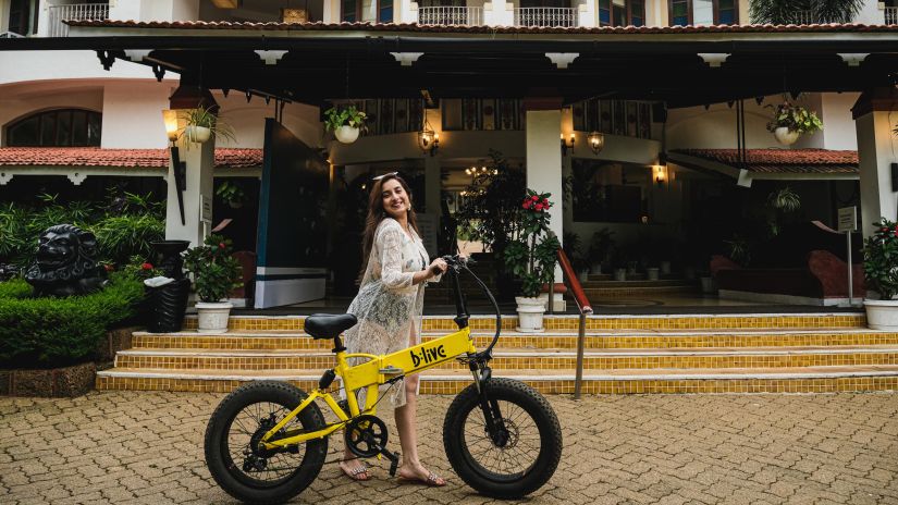 Heritage Village Goa - Image of a woman standing in front of the property facade with a bicycle next to her