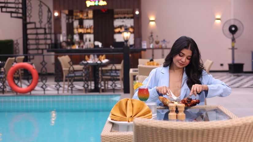 A woman feasting on food at her table next to the swimming pool at Skygrill restaurant with the bar counter in the background