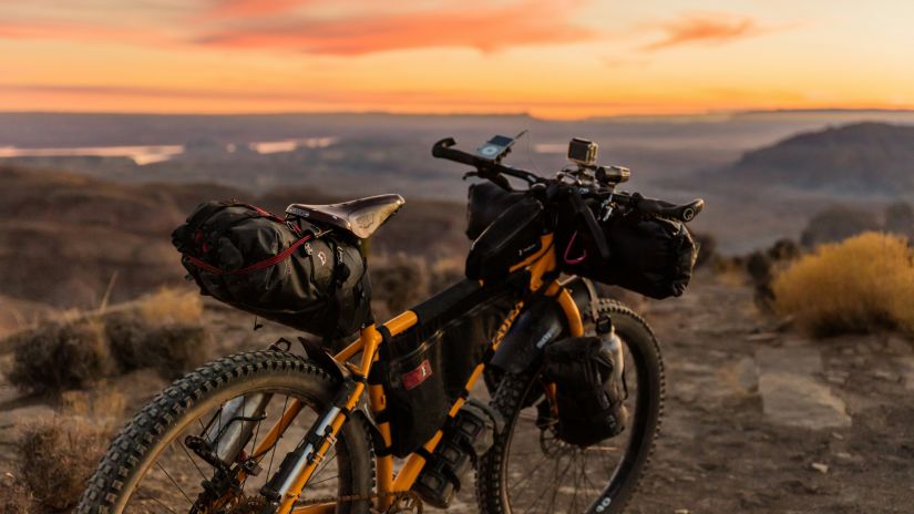 A bike loaded with gear stands silhouetted against a vibrant sunset in a desert landscape