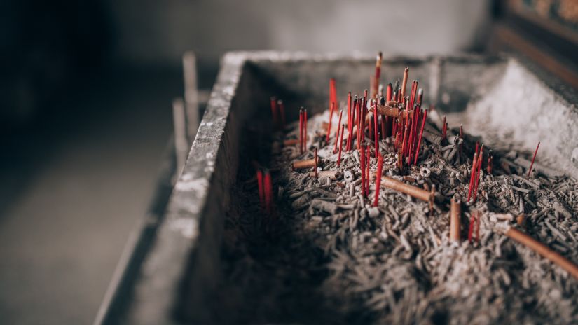 A flat rectangular container with ash and burnt incense sticks in it