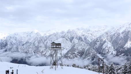 A watchtower on a hill in the midst of snow covered mountains