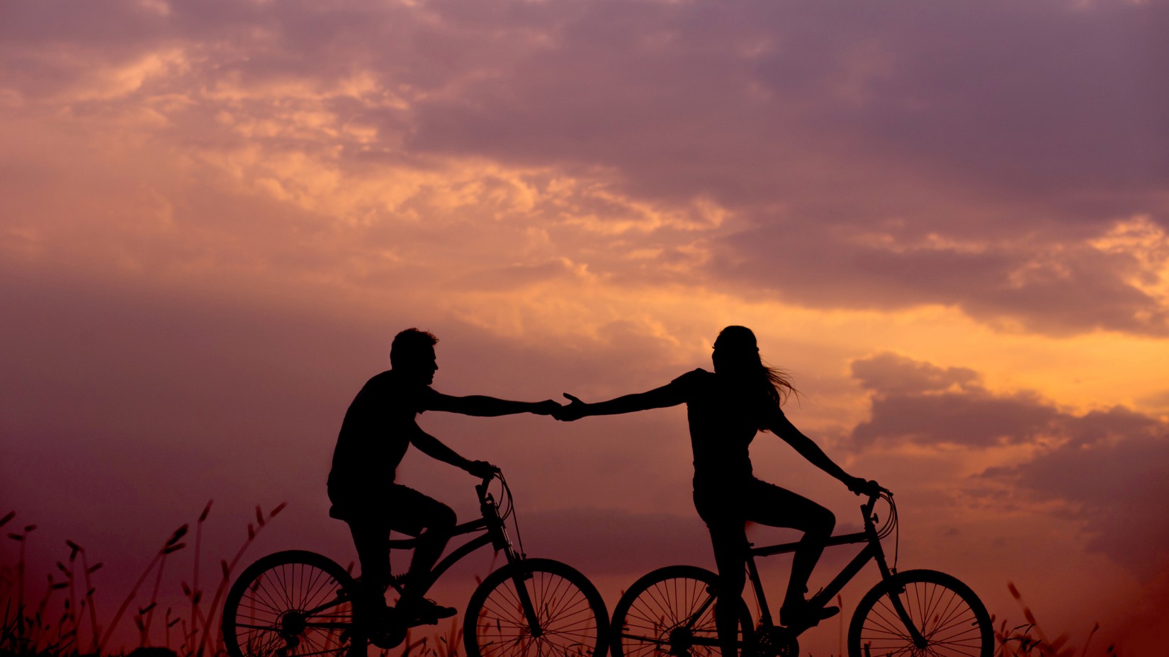 Couple holding hands while cycling with the evening sky in the background