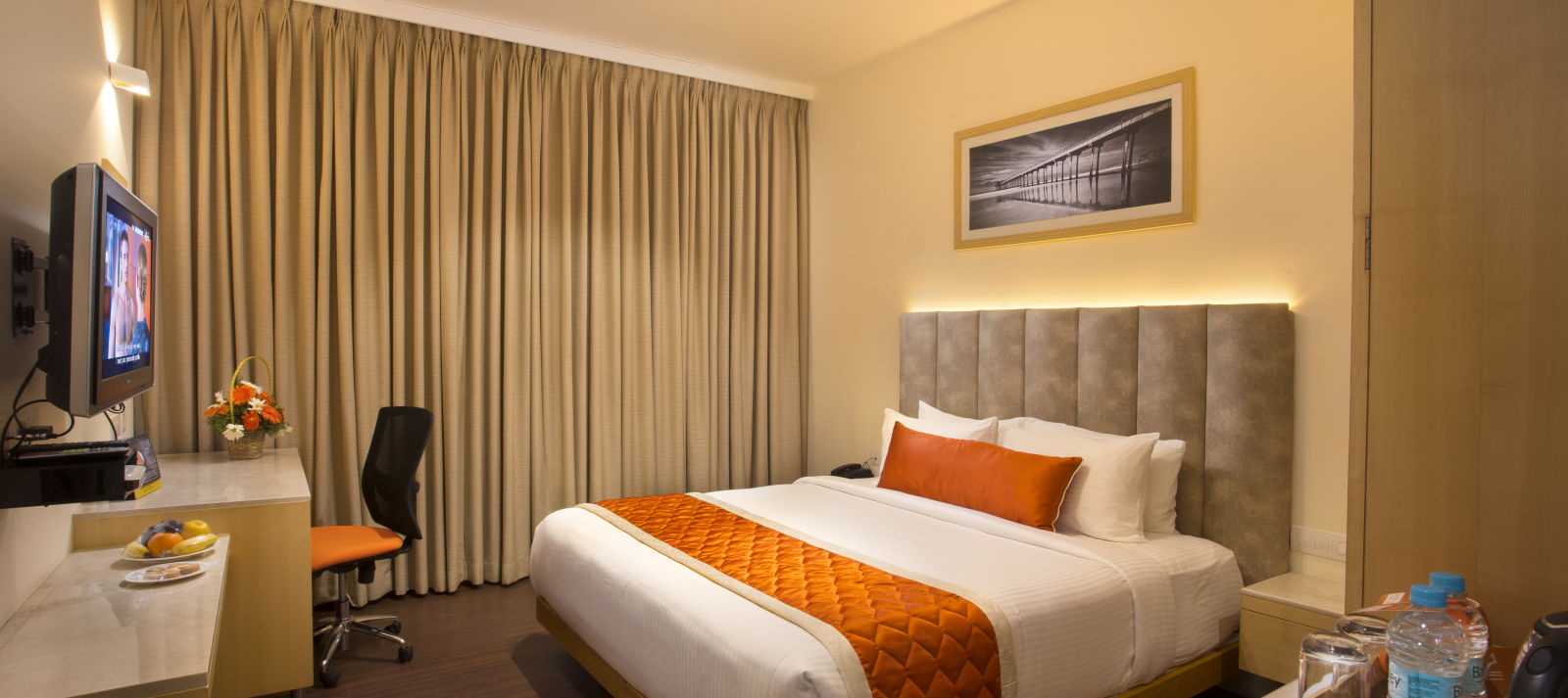 A cosy hotel room with a plush bed adorned with an orange bed runner, a work desk and a wall-mounted TV - Hotel Langford Keys by TGI, Shanti Nagar