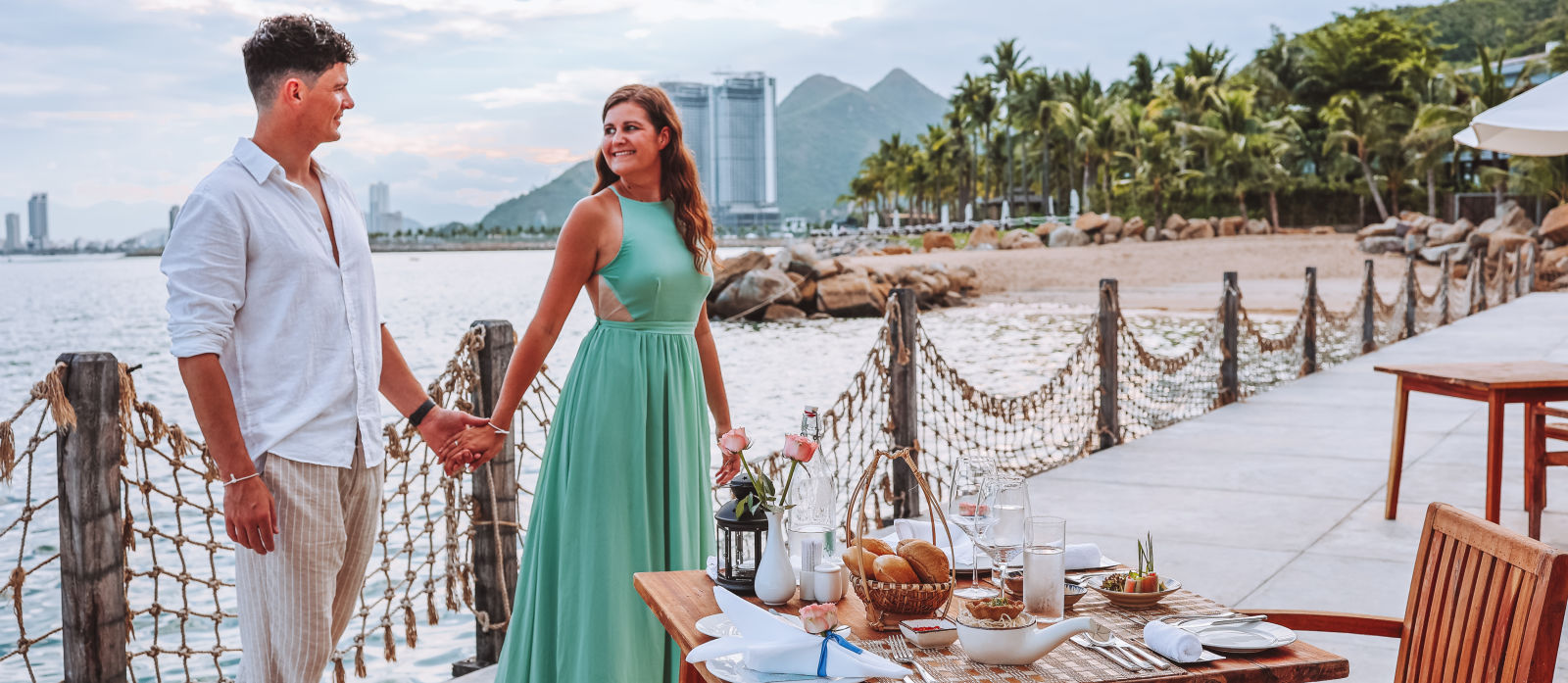 a couple hand in hand by the bay during daytime with views of the ocean, city and hills in the background