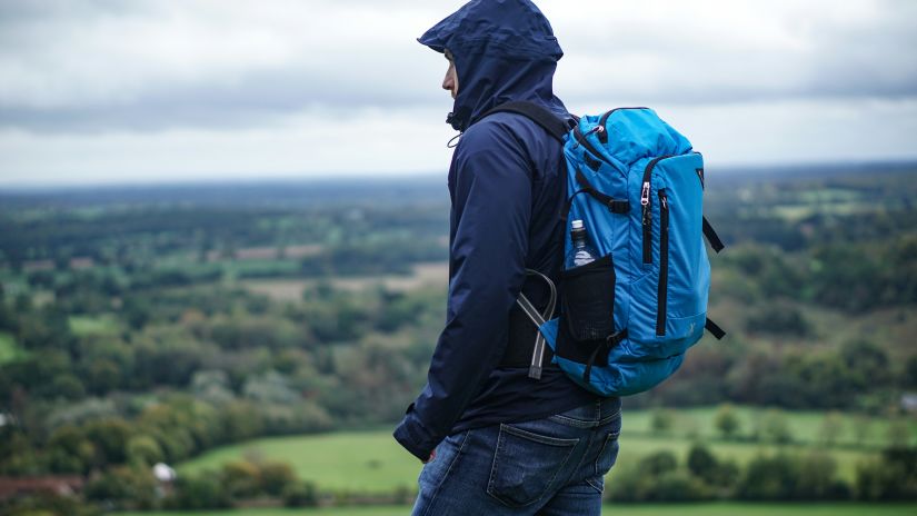 A man with a blue backpack gazes out over a lush green landscape from the viewpoint.