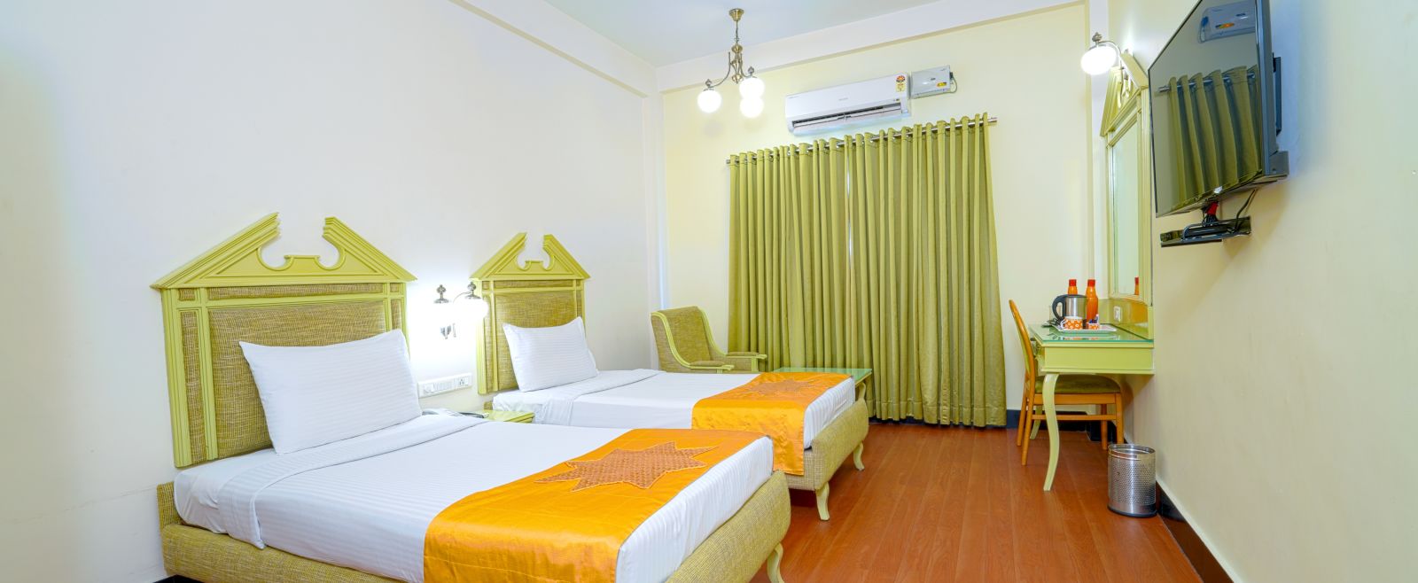 A twin hotel room with light wooden flooring, green headboard, and mustard accents, offering a cozy atmosphere. - Greens Inn - Cozy Accommodations