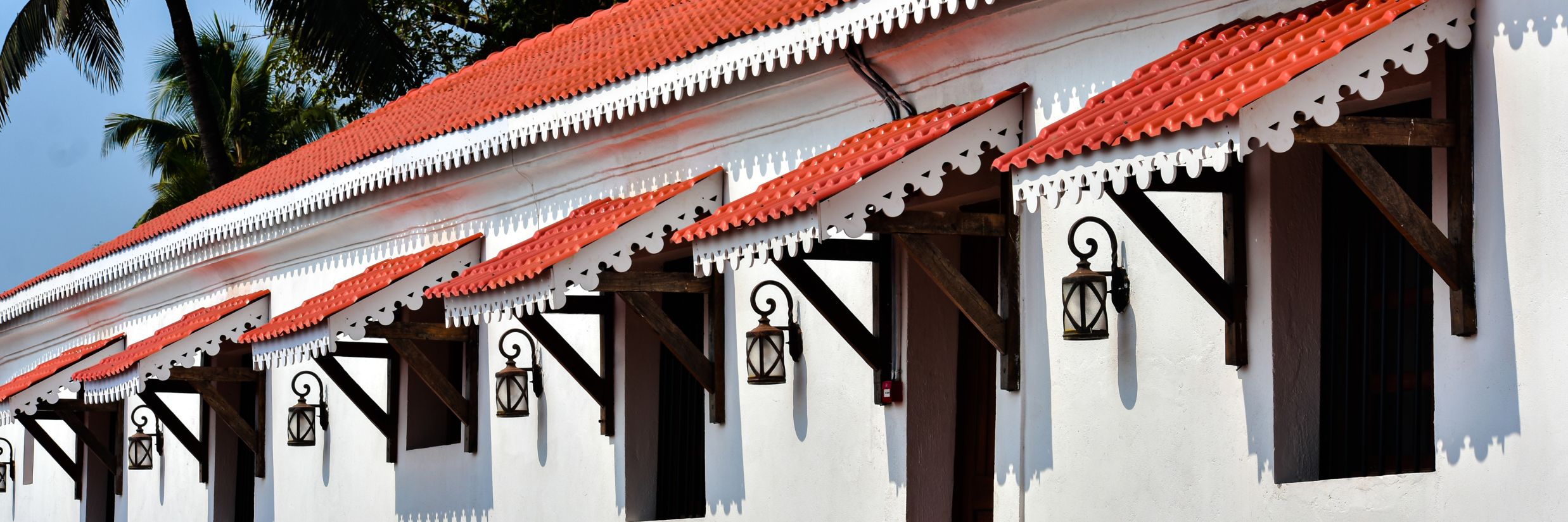 White building with red roof and coconut trees on side