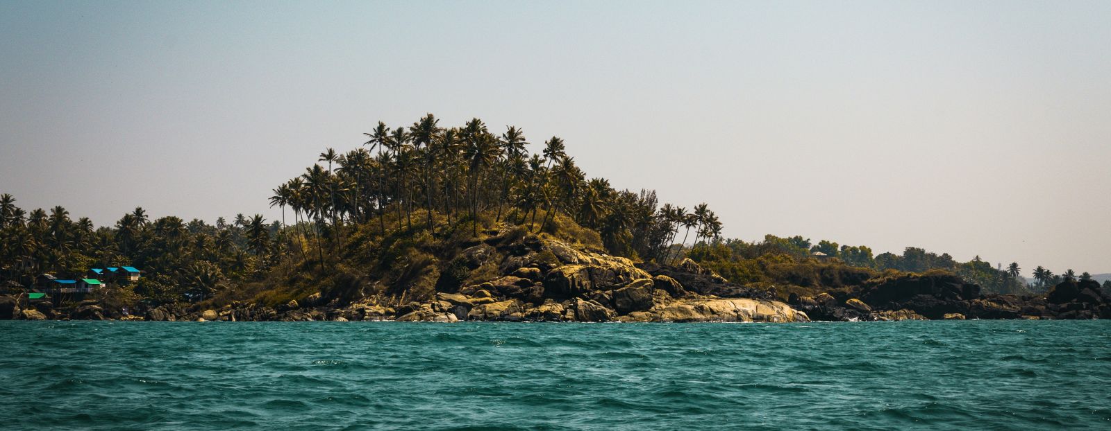 a view from the sea of palolem beach with trees and blue sky in the background