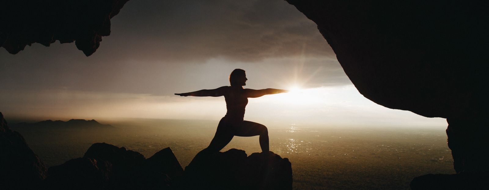 silhouette of a person doing yoga on top of a cliff during sunrise