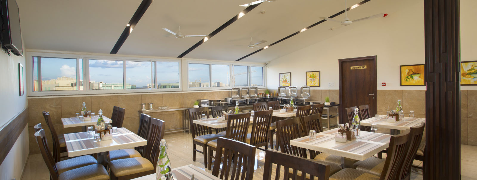 A hotel restaurant with wooden tables and chairs, large windows and ceiling fans - De Venetian by TGI, Brookefield