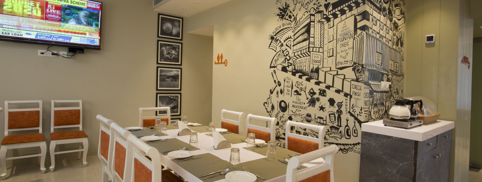 A cosy restaurant corner with a large wall mural, a buffet counter and a flat-screen TV showing news - Hotel Langford Keys by TGI, Shanti Nagar