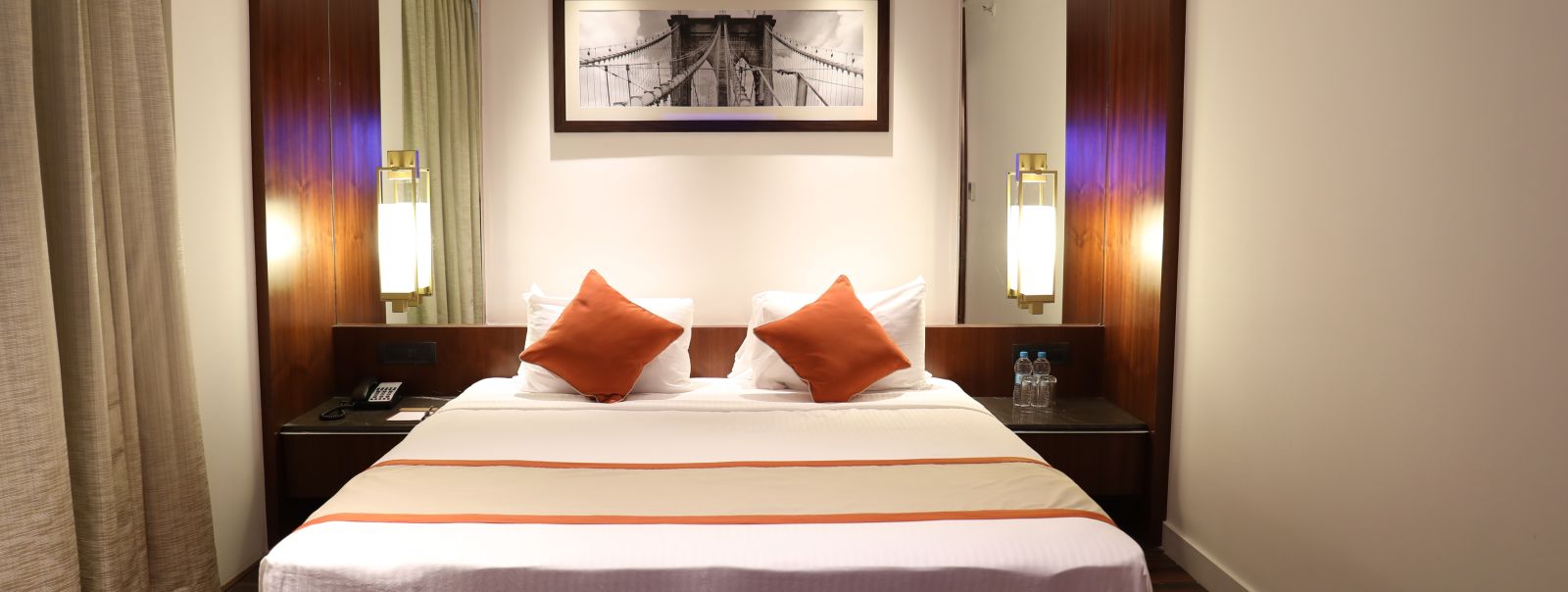 The front view of a hotel room with a large bed, white linens, burnt orange accents and a framed picture of a bridge above the headboard - Hotel Southend by TGI - Bommasandra, Bangalore