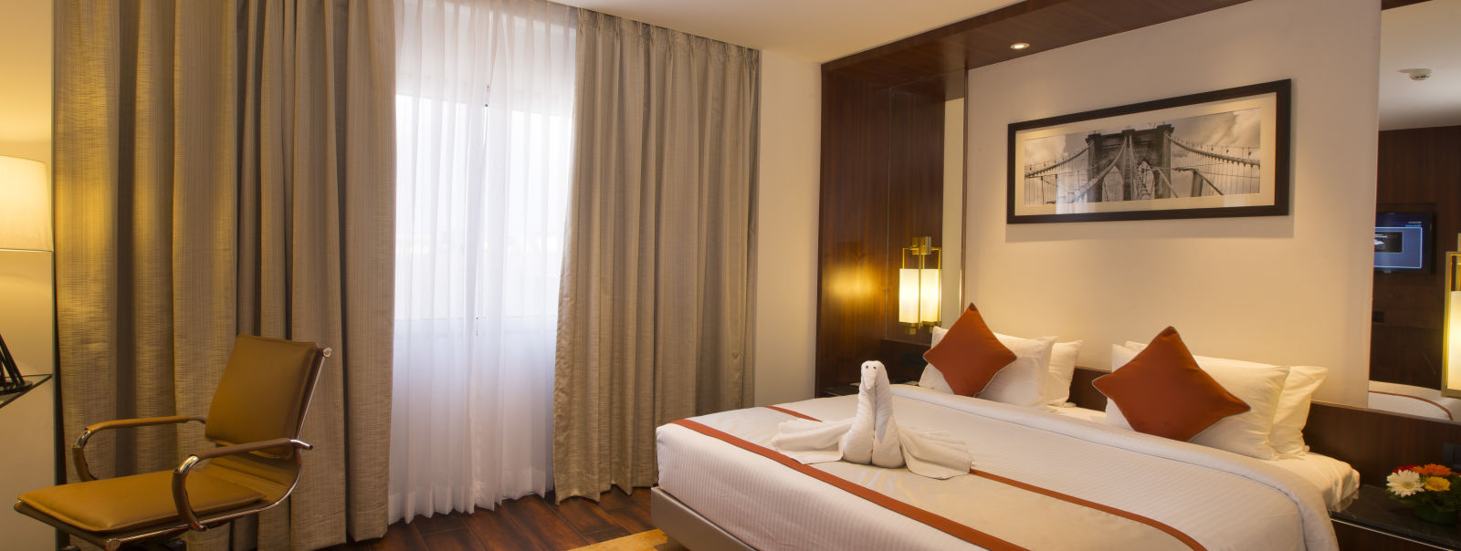 Another view of a hotel room with a large bed with white and orange linens, a brown office chair and sheer curtains over a window - Hotel Southend by TGI - Bommasandra, Bangalore