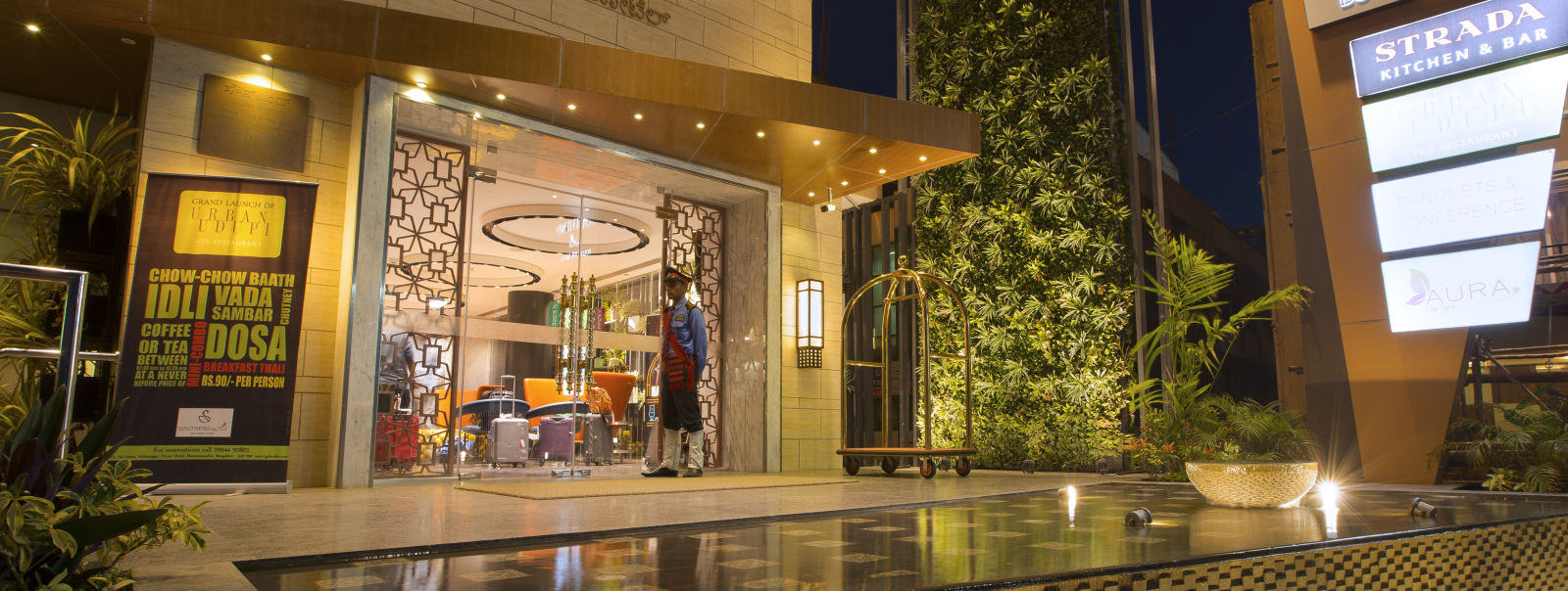 The exterior entrance of a hotel at dusk, featuring signage, a bellhop and a reflective water feature - Hotel Southend By TGI - Bommasandra, Bangalore