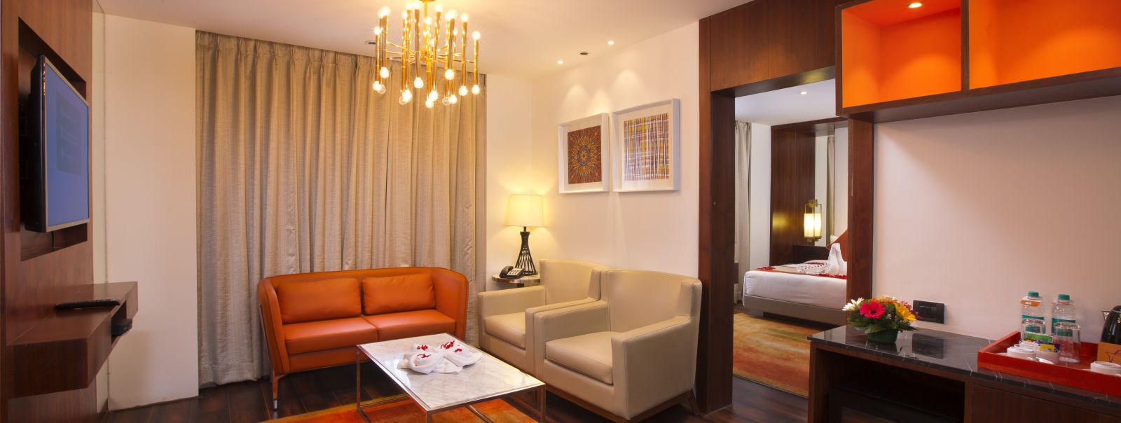 A hotel suite living area with a modern chandelier, orange leather sofa and a marble coffee table - Hotel Southend by TGI - Bommasandra, Bangalore