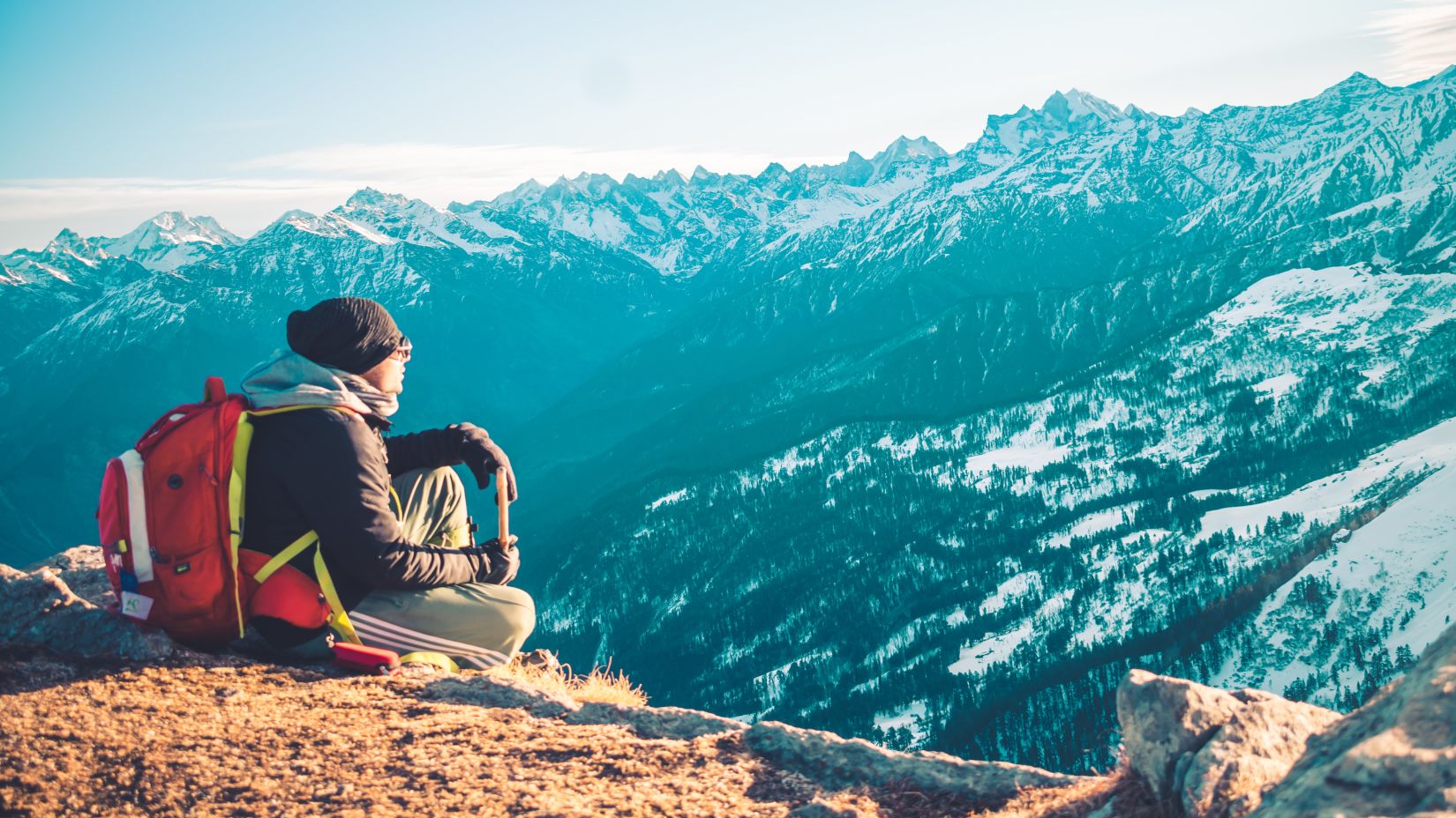 A person sitting on a mountain peak experiencing the breathtaking landscapes of Manali