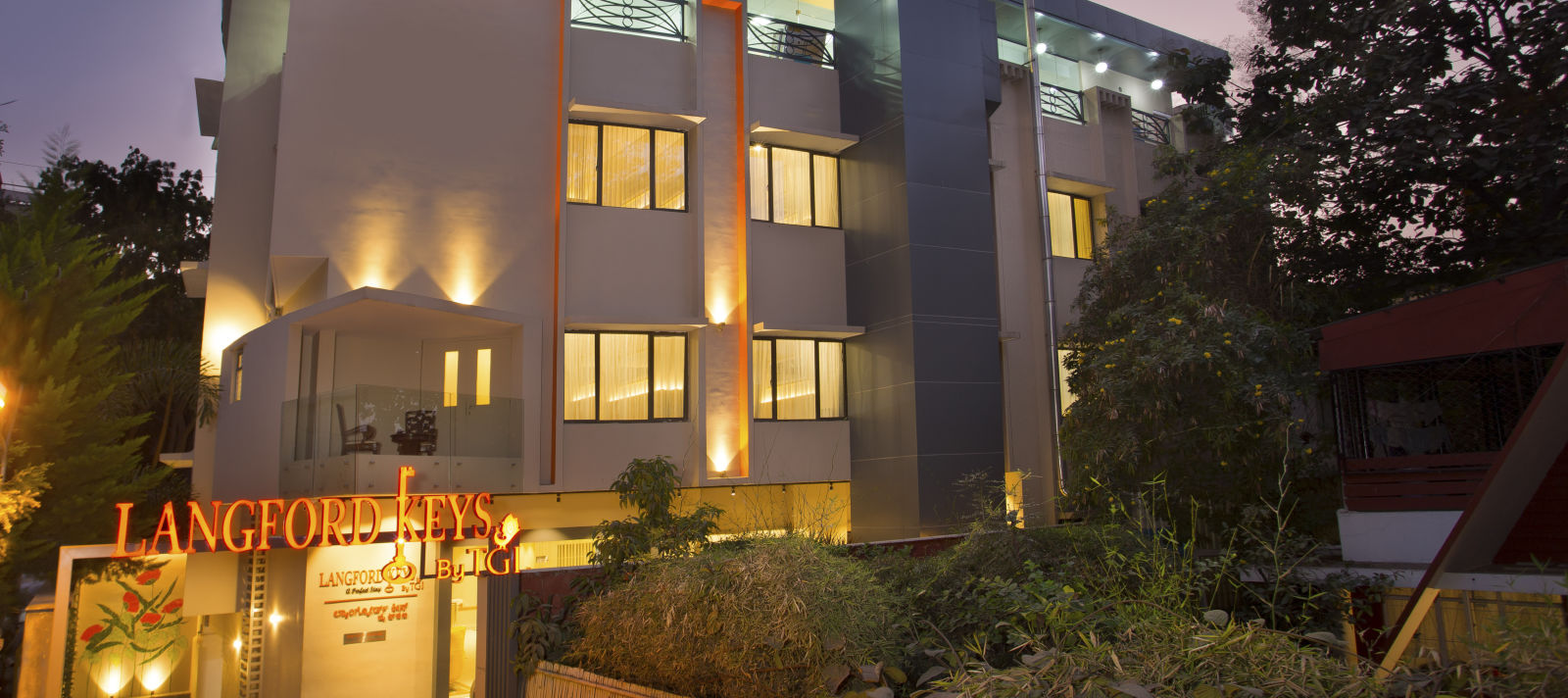 The exterior entrance of Langford Keys Hotel showing the signboard with reflective windows and modern architecture at dusk - Hotel Langford Keys by TGI, Shanti Nagar