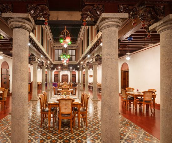 alt-text Elegant dining hall with vintage furniture and colorful floor tiles under a grand wooden ceiling at Chidambara Vilas Resort