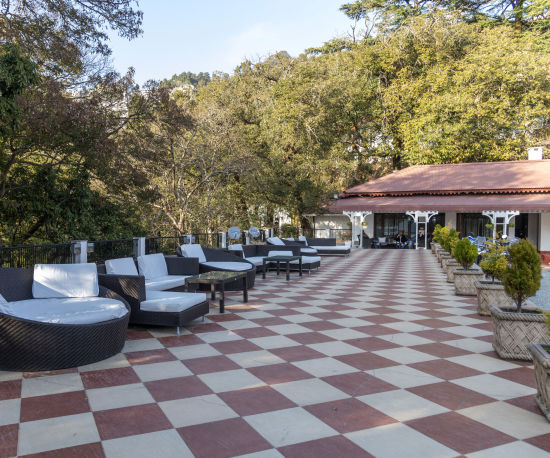 alt-text An outdoor seating area at The Claridges Nabha Residence in Mussoorie, characterized by comfortable, plush seating and encircled by a dense, lush green forest.